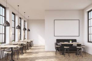 Cafe interior with a large sofa near a white wall, a row of tables with chairs near windows and a big horizontal poster on the wall, wooden floor. 3d rendering. Mock up.